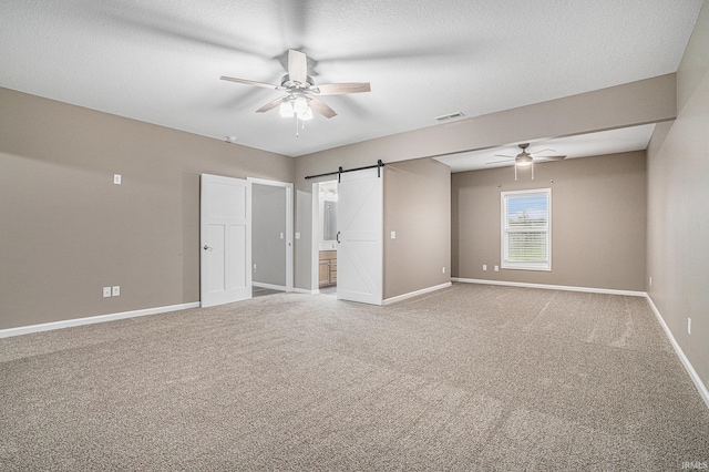 unfurnished bedroom featuring visible vents, baseboards, ensuite bathroom, light colored carpet, and a barn door
