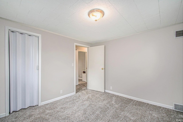 unfurnished bedroom with carpet flooring, visible vents, ornamental molding, and a closet