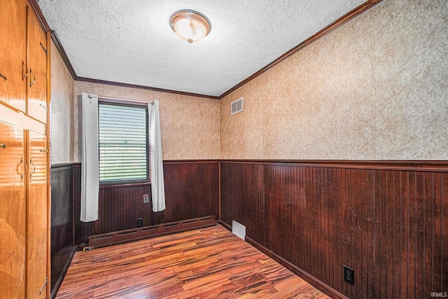 empty room featuring crown molding, baseboard heating, a textured ceiling, wood finished floors, and visible vents