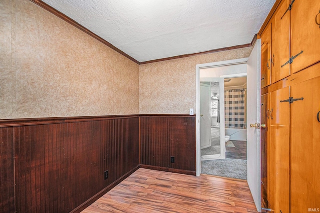 unfurnished room with a textured ceiling, wainscoting, wood walls, wood finished floors, and ornamental molding