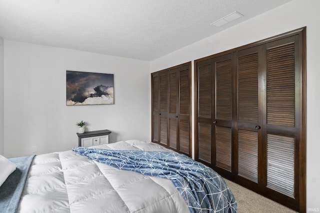 bedroom with visible vents, two closets, a textured ceiling, and light colored carpet