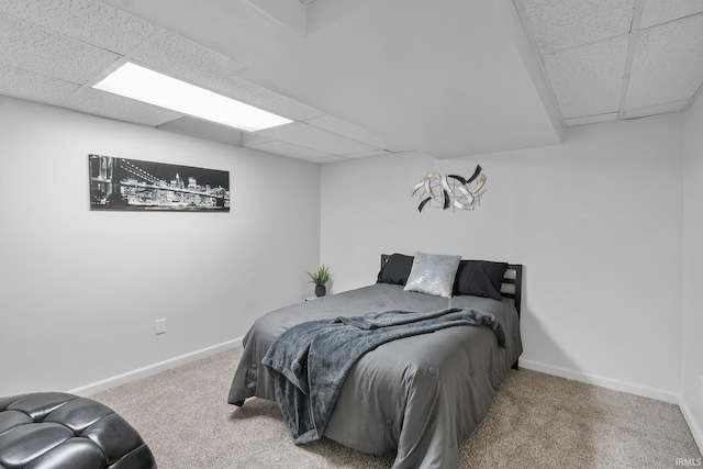 carpeted bedroom featuring baseboards and a drop ceiling