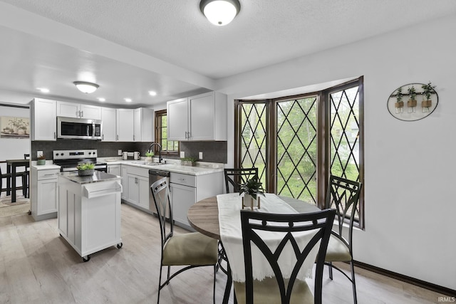 kitchen with light wood-style floors, a center island, tasteful backsplash, a sink, and stainless steel appliances