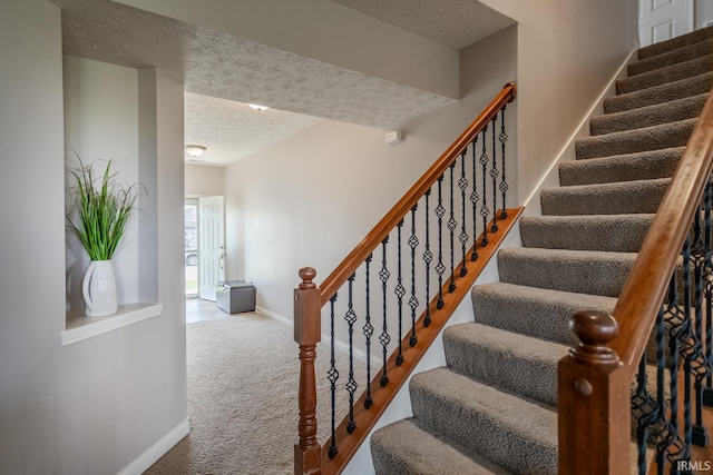 stairway with carpet floors, baseboards, and a textured ceiling