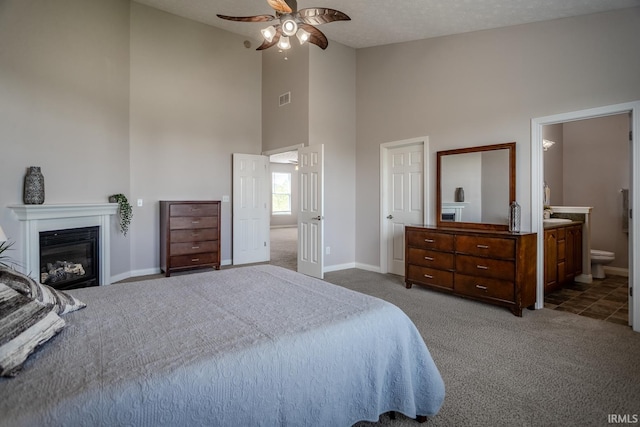carpeted bedroom featuring visible vents, a glass covered fireplace, baseboards, high vaulted ceiling, and connected bathroom