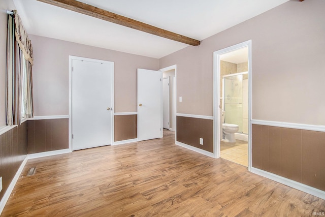 unfurnished bedroom with connected bathroom, beam ceiling, visible vents, and wood finished floors