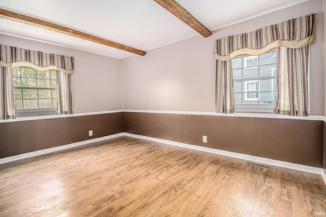 empty room with baseboards, visible vents, beam ceiling, and wood finished floors