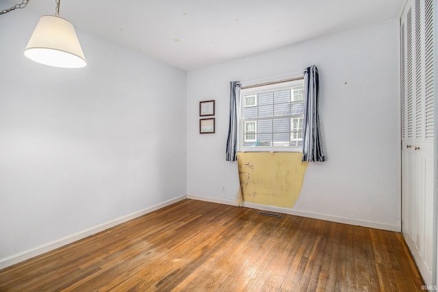 spare room featuring wood-type flooring, baseboards, and visible vents