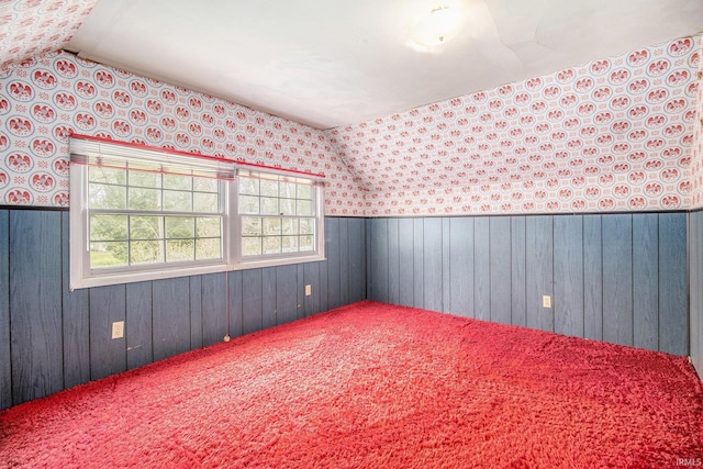 interior space with a wainscoted wall, wood walls, wallpapered walls, and lofted ceiling