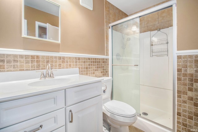 full bath featuring tile walls, wainscoting, a shower stall, vanity, and toilet