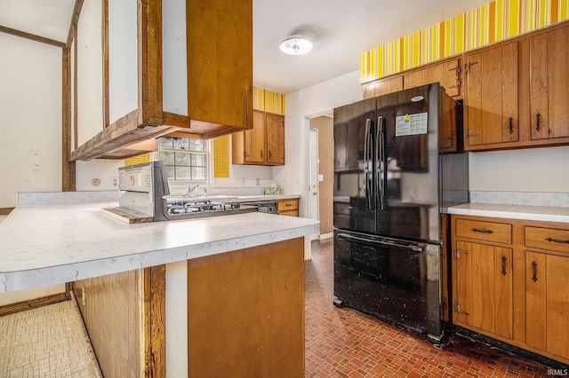 kitchen featuring brown cabinetry, freestanding refrigerator, a peninsula, and light countertops