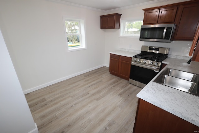 kitchen featuring crown molding, light countertops, a sink, light wood-style flooring, and stainless steel appliances