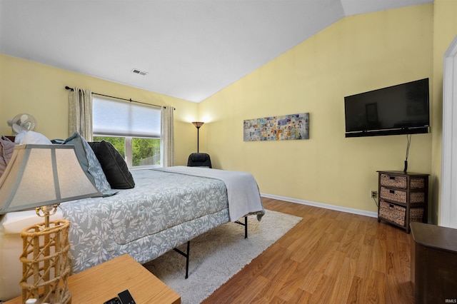 bedroom with baseboards, wood finished floors, vaulted ceiling, and visible vents
