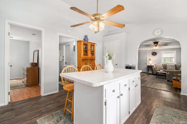 kitchen featuring ceiling fan, arched walkways, light countertops, white cabinets, and dark wood-type flooring