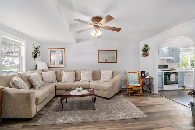 living area with arched walkways, a ceiling fan, and dark wood-type flooring