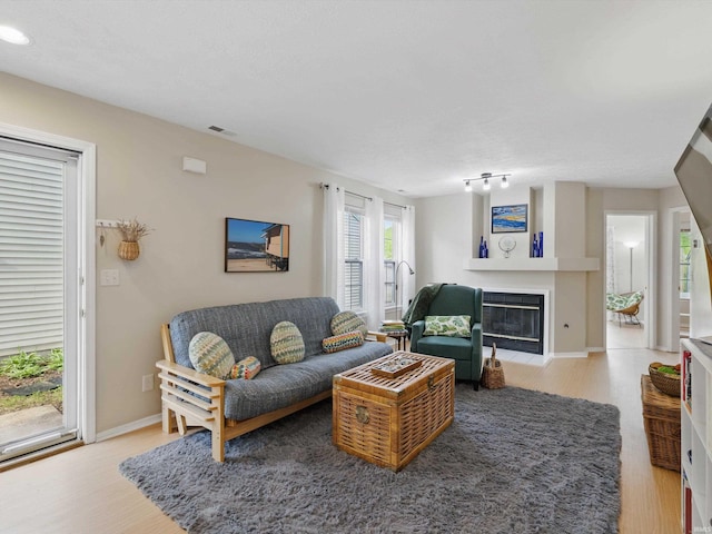 living room featuring light wood-type flooring, a fireplace with flush hearth, baseboards, and visible vents