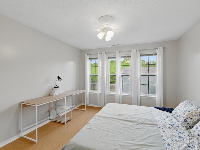 bedroom with baseboards, a textured ceiling, and wood finished floors