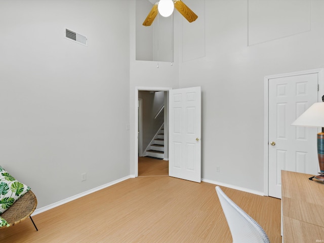 interior space with visible vents, baseboards, ceiling fan, a high ceiling, and light wood-type flooring