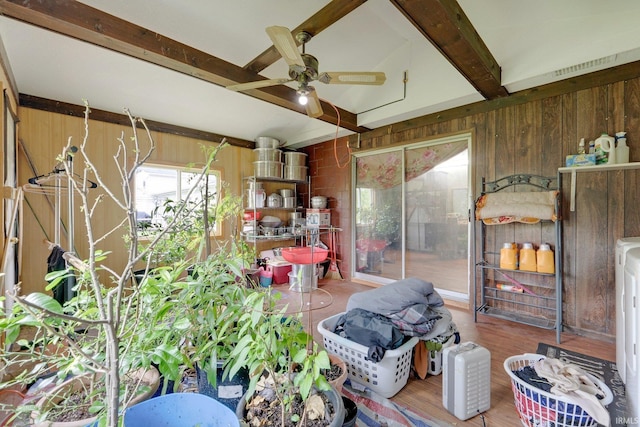interior space with wooden walls, a ceiling fan, beamed ceiling, and wood finished floors