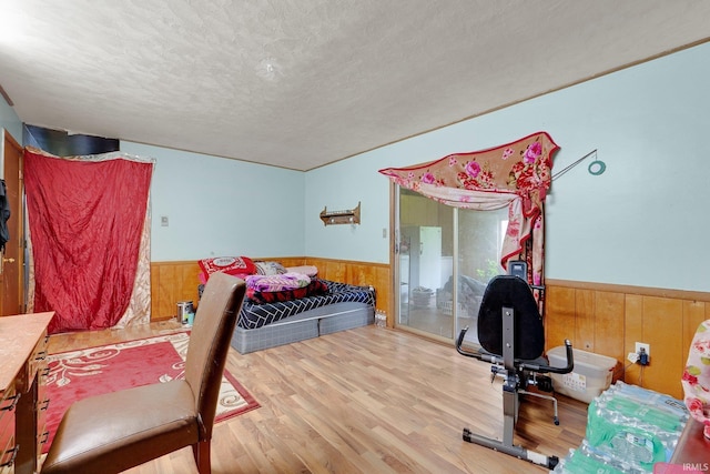 bedroom with wooden walls, a wainscoted wall, a textured ceiling, and wood finished floors
