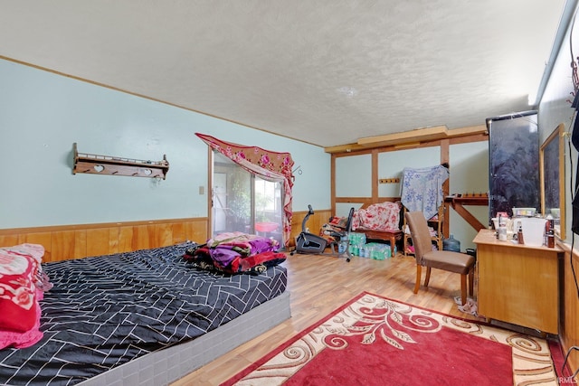 bedroom featuring a wainscoted wall, a textured ceiling, wood walls, and wood finished floors