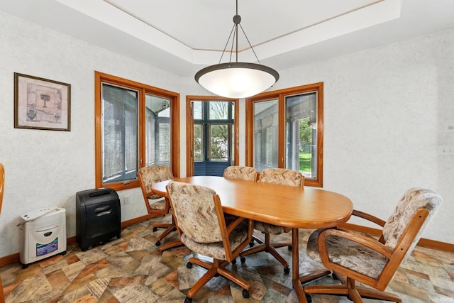 dining space with baseboards, stone finish flooring, and a tray ceiling