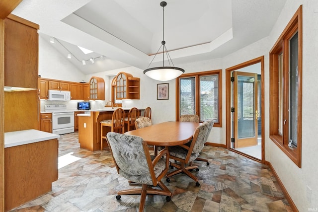 dining room with vaulted ceiling with skylight, baseboards, stone finish floor, and a tray ceiling