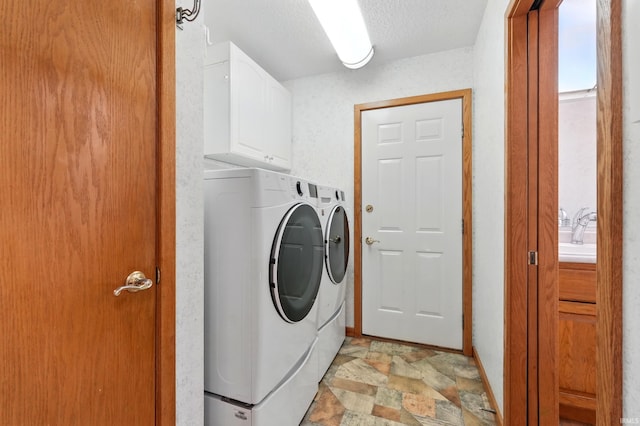 washroom featuring washer and dryer, baseboards, stone finish floor, a textured ceiling, and cabinet space
