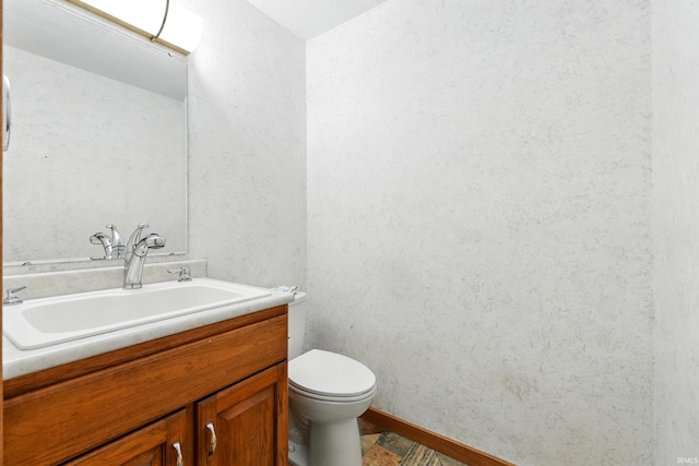 bathroom featuring vanity, baseboards, a textured wall, and toilet