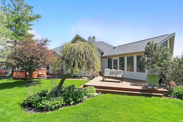 rear view of house with a lawn, a shingled roof, a wooden deck, and a chimney