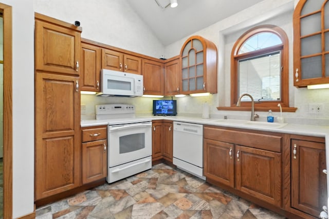 kitchen with brown cabinetry, a sink, vaulted ceiling, and white appliances
