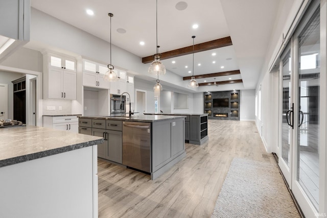 kitchen featuring stainless steel dishwasher, a kitchen island with sink, dark countertops, light wood-style flooring, and gray cabinetry