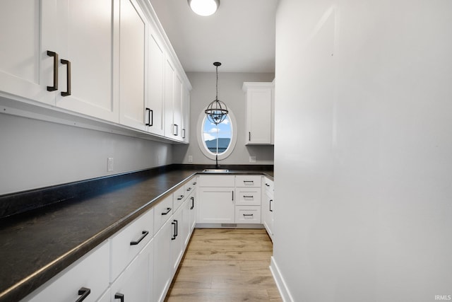 kitchen featuring dark countertops, hanging light fixtures, a sink, white cabinetry, and light wood-type flooring