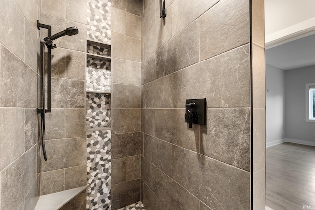 bathroom with baseboards, a tile shower, and wood finished floors