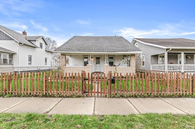 view of front facade with roof with shingles, brick siding, a gate, a porch, and a fenced front yard