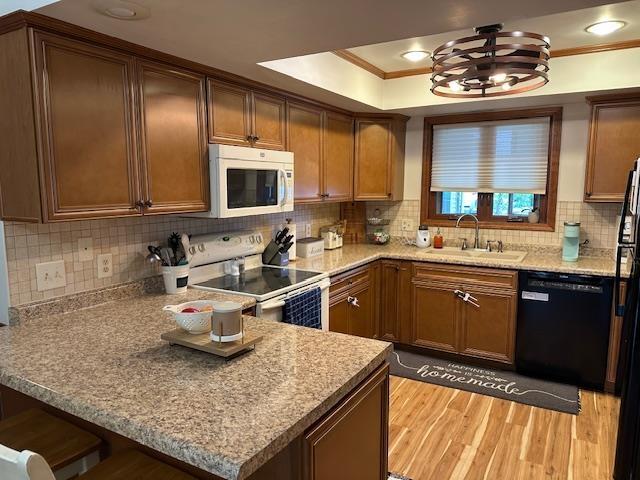 8615 Timbermill Pl, Fort Wayne, IN 46804 - kitchen featuring white appliances, a sink, light wood-style flooring, a peninsula, and a tray ceiling