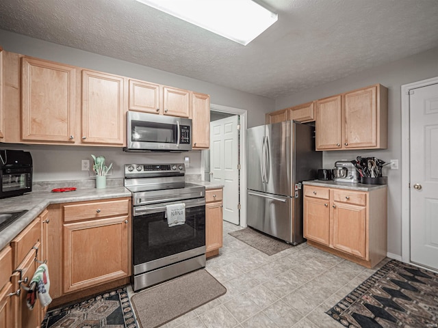 kitchen with light countertops, a textured ceiling, light brown cabinetry, and stainless steel appliances