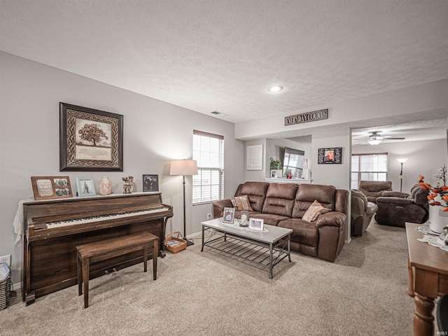 living area featuring light colored carpet, a textured ceiling, a ceiling fan, baseboards, and visible vents