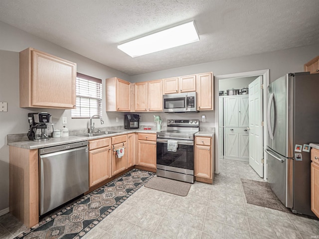 kitchen with a sink, light brown cabinets, light countertops, a textured ceiling, and stainless steel appliances