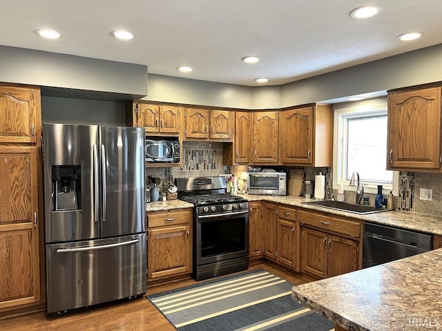 kitchen featuring brown cabinets, backsplash, appliances with stainless steel finishes, and a sink