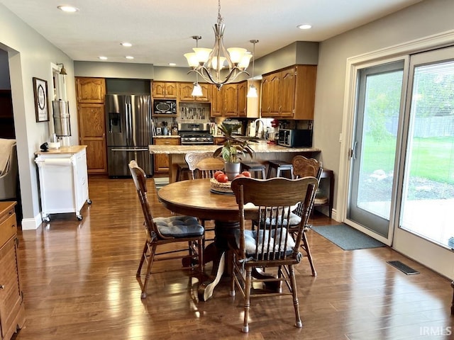 dining area featuring visible vents, dark wood finished floors, a healthy amount of sunlight, and an inviting chandelier