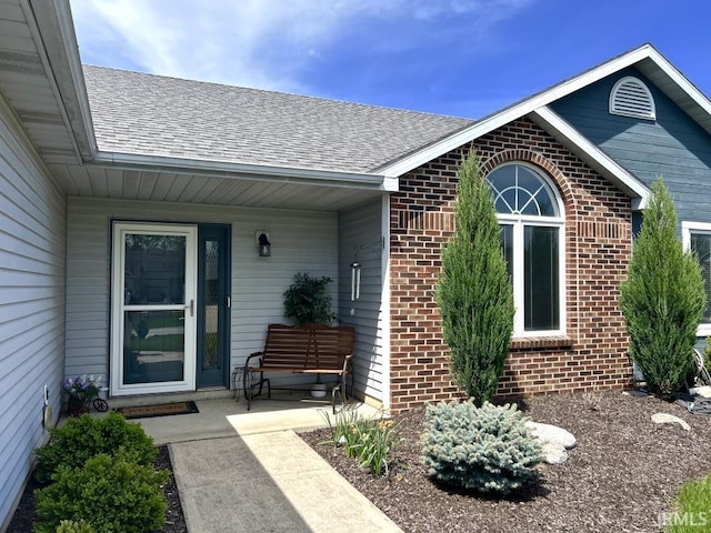 doorway to property with roof with shingles, covered porch, and brick siding
