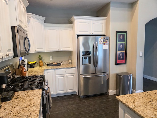 kitchen with baseboards, white cabinetry, arched walkways, dark wood finished floors, and stainless steel appliances