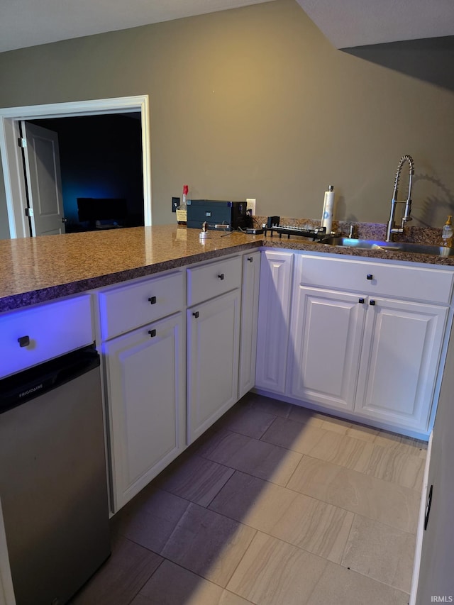 kitchen featuring a sink, dishwashing machine, light tile patterned flooring, and white cabinets