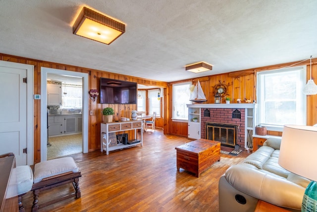 living area with a brick fireplace, a textured ceiling, wood walls, and wood finished floors