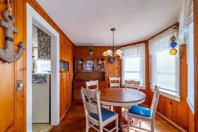 dining space with wooden walls, ornamental molding, wood finished floors, and a notable chandelier