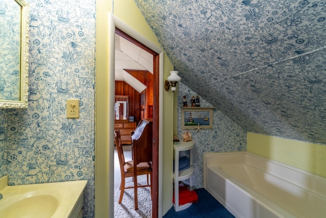 bathroom with a washtub, wallpapered walls, vaulted ceiling, and a sink