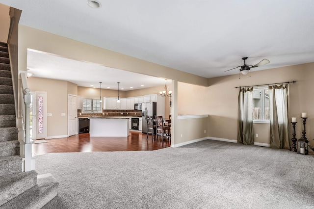 unfurnished living room featuring dark carpet, ceiling fan with notable chandelier, stairs, recessed lighting, and baseboards