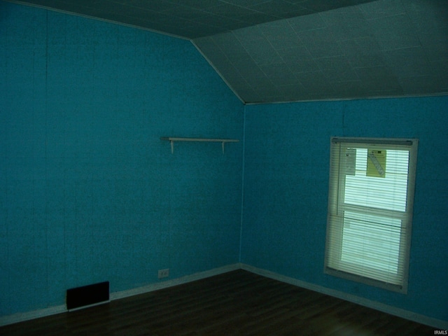 empty room with baseboards, vaulted ceiling, dark wood-style flooring, and visible vents