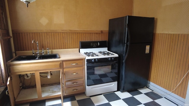 kitchen with freestanding refrigerator, light floors, gas range, a wainscoted wall, and a sink